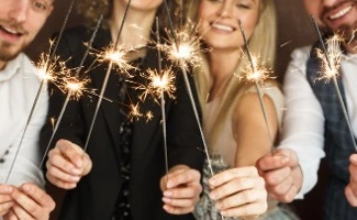 Grupo de personas sosteniendo bengalas encendidas y sonriendo, celebrando juntas en un ambiente festivo.