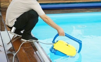 Persona realizando tareas de mantenimiento y limpieza en una piscina comunitaria utilizando un equipo automático de limpieza.
