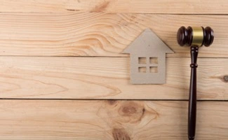 Mazo judicial junto a una figura de casa sobre fondo de madera, simbolizando la legislación y la propiedad inmobiliaria.